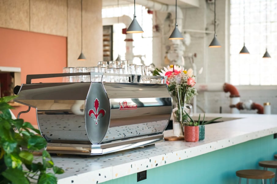 Photo of a shiny silver La Marzocco espresso machine on top of a counter in a bright, hip-looking coffee shop